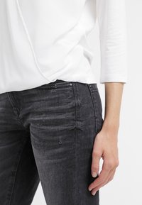 Un haut à manches longues blanc associé à un jean gris foncé avec une texture subtile, un léger effet usé et un design classique à cinq poches.