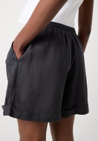 Shorts neri in lino con vita elasticizzata, tasche laterali e orlo arrotolato. Texture morbida e vestibilità comoda.