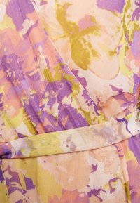 Tissu léger avec imprimé floral pastel en violet, pêche, jaune et vert, présentant un style portefeuille avec un chevauchement et une ceinture assortie.