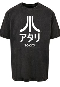 Schwarzes Baumwoll-T-Shirt mit kurzen Ärmeln, das ein großes weißes Atari-Logo in stilisierten Buchstaben und darunter das Wort "TOKYO" zeigt.