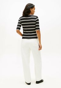 Top de rayas en blanco y negro con canalé y mangas cortas, combinado con pantalones anchos blancos, visto desde atrás, con zapatos negros.