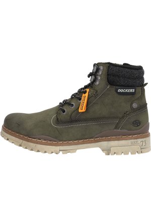Botas de tobillo de ante verde oscuro con un cuello de tela gris, ojales de metal negro, etiqueta naranja y suela de goma beige resistente.