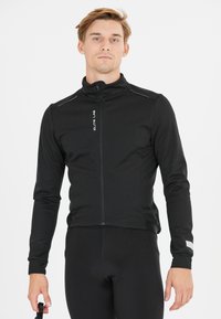Veste noire zippée avec un col montant, fabriquée à partir d'un tissu texturé. Présente des bandes réfléchissantes aux épaules et un logo à l'avant.