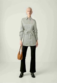 Gray button-up shirt with long sleeves, a tied waist, paired with black flared pants and a brown shoulder bag. Black heeled boots complete the look.