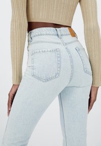 Jeans de talle alto en azul claro con una textura ligeramente deslavada, con bolsillos de parche y costuras contrastantes. Junto a una blusa de punto beige.