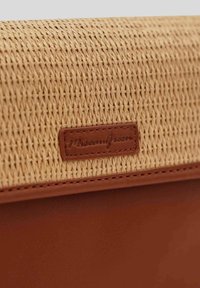 Extérieur en paille tissée avec une base en cuir beige et des détails en cuir. Présente une petite étiquette de marque embossée sur un patch en cuir.