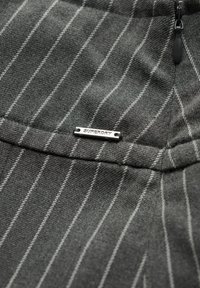 Grijze stof met een fijn gestreept patroon, voorzien van een klein zilveren Superdry logo label. De textuur lijkt zacht en licht gestructureerd.
