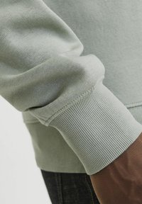 Világoszöld pulóver, bordás mandzsettával. Az anyag lágy és sima, finom textúrával rendelkezik, és kényelmes illeszkedést biztosít.