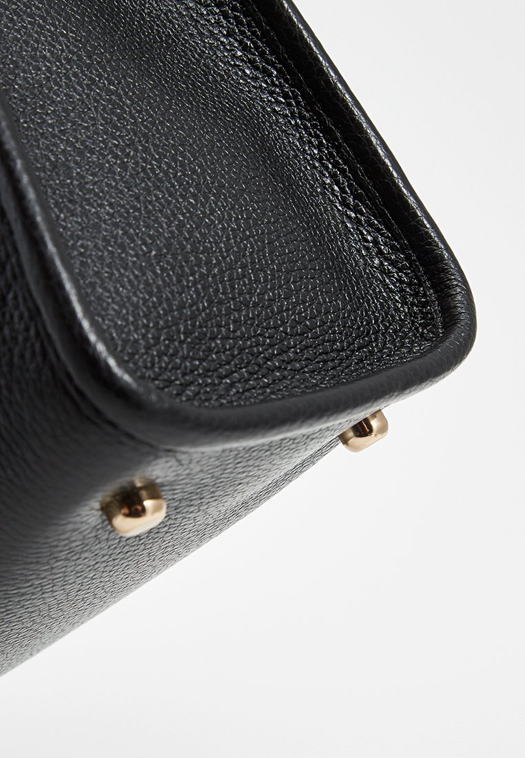 Bolso de piel negra con un acabado texturizado, que presenta detalles en dorado y pies protectores en la base para mayor estabilidad.