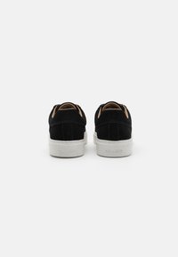 Black suede sneakers with a white rubber sole, featuring a minimal design, round toe, and subtle Calvin Klein branding on the heel.