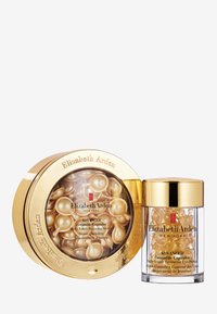 Conteneur circulaire doré avec un couvercle transparent contenant plusieurs capsules dorées. À côté, une bouteille claire avec un capuchon doré présentant des capsules similaires.