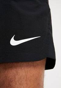 Svarta träningsshorts med en vit Nike-logotyp på vänster sida, tillverkade av ett slätt och lätt material med en sicksackad fåll.