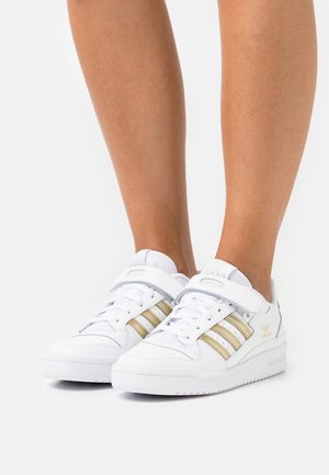 Białe sneakersy z złotymi i srebrnymi trzema paskami, skórzana cholewka, wyłożony język i pasek na rzep. Teksturowana podeszwa dla lepszej przyczepności.