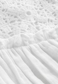 White garment featuring intricate lace detailing at the top and gathered fabric below, with a soft, textured finish.