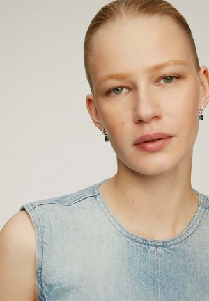 Top sin mangas de denim azul claro con un escote redondo. Textura suave y detalles de costura mínimos, combinado con pendientes sutiles.