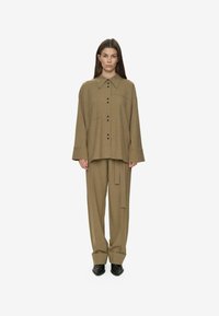 Camisa de gran tamaño en verde oliva, con cuello puntiagudo y botones negros, combinada con pantalones a medida a juego, que presentan un cinturón anudado y piernas anchas.