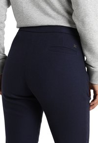 Pantalons ajustés bleu marine avec un tissage texturé, dotés d'une poche arrière et d'un devant plat. Assortis à un haut gris à manches longues.