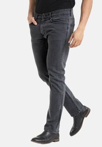 Jeans slim fit gris foncé en denim, avec un design classique à cinq poches et une fermeture éclair avec un bouton. Portés avec des bottes en cuir noires.