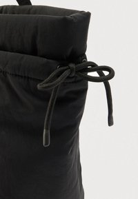 Sac matelassé noir avec une surface douce et texturée et une fermeture à cordon coulissant avec embouts en plastique noir, conçu pour un réglage sécurisé en haut.