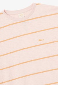 T-shirt rosa chiaro con sottili strisce arancioni orizzontali. Caratterizzato da un collo rotondo e un piccolo logo dorato sul petto. Tessuto morbido e testurizzato.