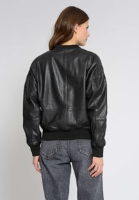 Svart läderflygjacka med ribbad krage och ärmar, med en avslappnad passform och slät yta. Bärs med grå högmidjade jeans.