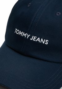 Granatowa czapka baseballowa z bawełny, z wygiętą daszkiem i białym, haftowanym logo "TOMMY JEANS" z przodu.