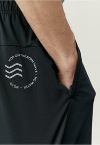 Fekete sportpantalón elasztikus derekkal és oldalzsebbel. Az oldalon egy kör alakú szürke grafika látható szöveges kiemelésekkel.