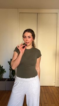 Femme en vêtements décontractés parlant dans un petit microphone dans une pièce avec des plantes et des portes d'armoire fermées en arrière-plan.