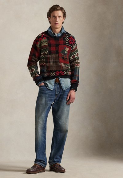 Stickad tröja med flerfärgade mönster i rött, grönt och brunt. Lager-på-lager över en ljusblå jeansskjorta. Bärs med blekta blå jeans och bruna skor.