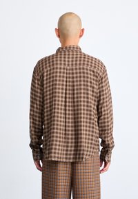 Brown plaid shirt with a button-down collar, featuring long sleeves and a relaxed fit. The fabric displays a soft texture and subtle sheen.