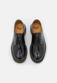 Černé lakované kožené boty s kulatou špičkou, dvěma dírkami, žlutým prošíváním, šněrováním a robustní texturovanou podrážkou.