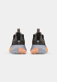 Een paar moderne sportschoenen met bruin mesh bovenwerk, zwarte accenten en oranje en grijze chunky zolen, van achteren weergegeven op een witte achtergrond.