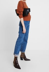 Brauner Strickpullover, blaue locker sitzende Jeans und schwarze Ledertasche. Braun-beige gemusterte Stiefeletten mit spitzen Zehen und Blockabsätzen.