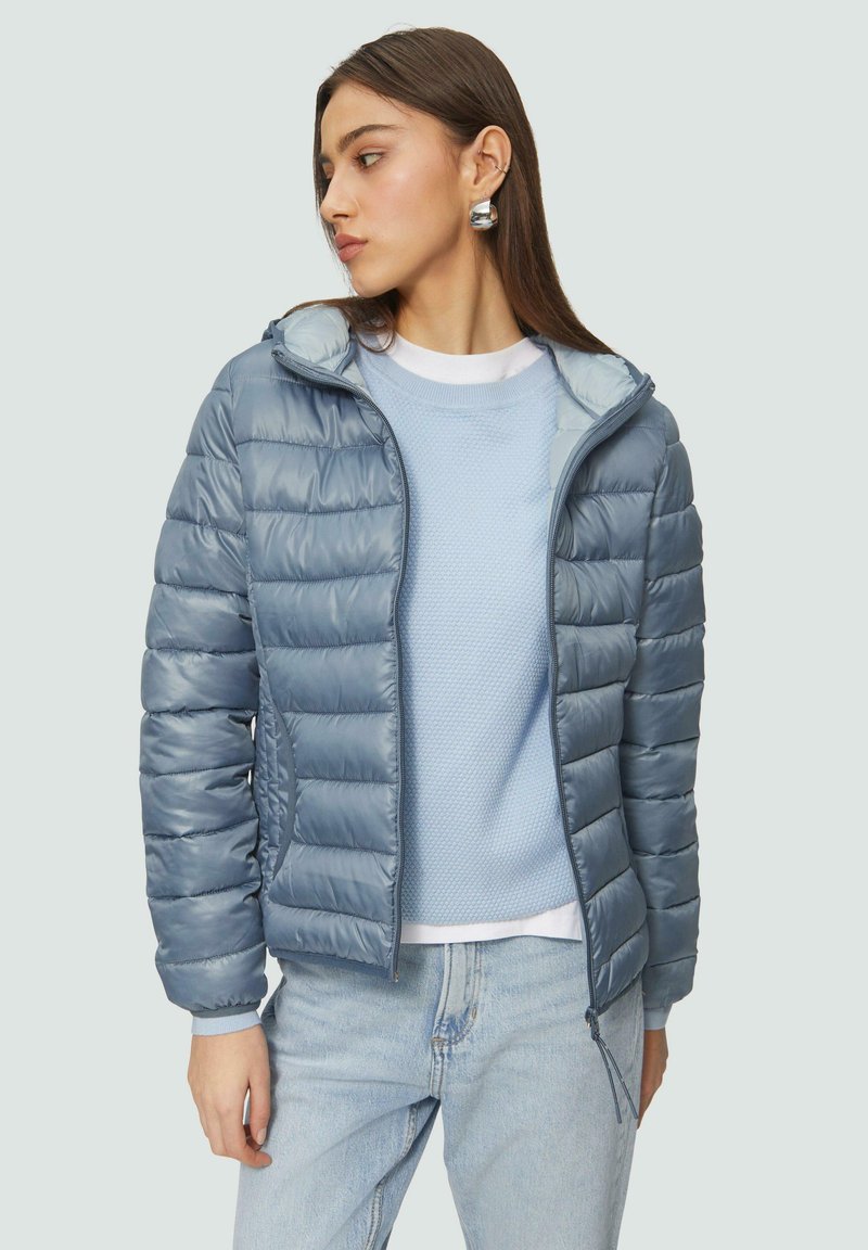 Helle blaue Daunenjacke mit horizontalem Steppdesign, ausgestattet mit einer Kapuze, Reißverschluss und seitlichen Taschen, über einem strukturierten blauen Pullover getragen.