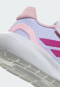 Violets tīkla sporta apavi ar rozā akcentiem; tām ir teksturēta balta zole un trīs rozā svītras sānos.