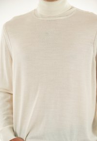 Maglione a collo alto di un leggero color crema, realizzato in tessuto morbido, con maniche lunghe e una vestibilità aderente caratterizzata da una texture liscia.