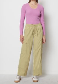 Haut rose à manches longues côtelé associé à un pantalon cargo large vert clair avec une taille élastique et des poches latérales. Baskets blanches avec des accents.