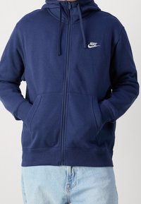 Sudadera con cremallera de color navy, hecha de una suave mezcla de algodón, que cuenta con un bolsillo tipo canguro, capucha con cordón y un logo bordado en el pecho.
