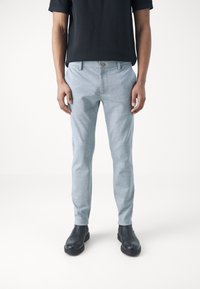 Pantalones ajustados gris claro con una textura sutil, que cuentan con un cierre de botón, trabillas para cinturón y un corte slim, combinados con botines negros.