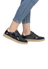 Schwarze Lackledersneaker mit strukturiertem Finish und beiger Gummisohle. Merkmale sind ein metallisch goldener Absatz und passende Schnürsenkel.