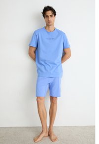 Svetlo modré bavlnené tričko s krátkymi rukávmi a okrúhlym výstrihom, doplnené o zodpovedajúce šortky. Logo "Calvin Klein" kontrastne vyšívané na tričku.