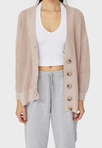 Beige stickad cardigan med lös passform, som har en djup halsringning, långa ärmar och fem stora bruna knappar fram.