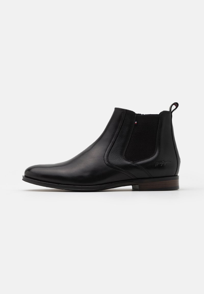 Bottine Chelsea en cuir noir avec panneau latéral élastique, petit talon en bois, languette à l'arrière et logo discret sur le côté.