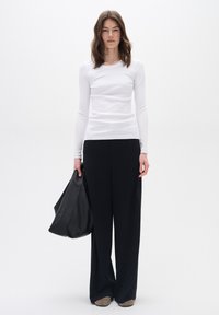 Vit långärmad ribbad topp kombinerad med svarta vida byxor, håller en svart läderväska. Skor i neutrala färger fulländar outfiten.