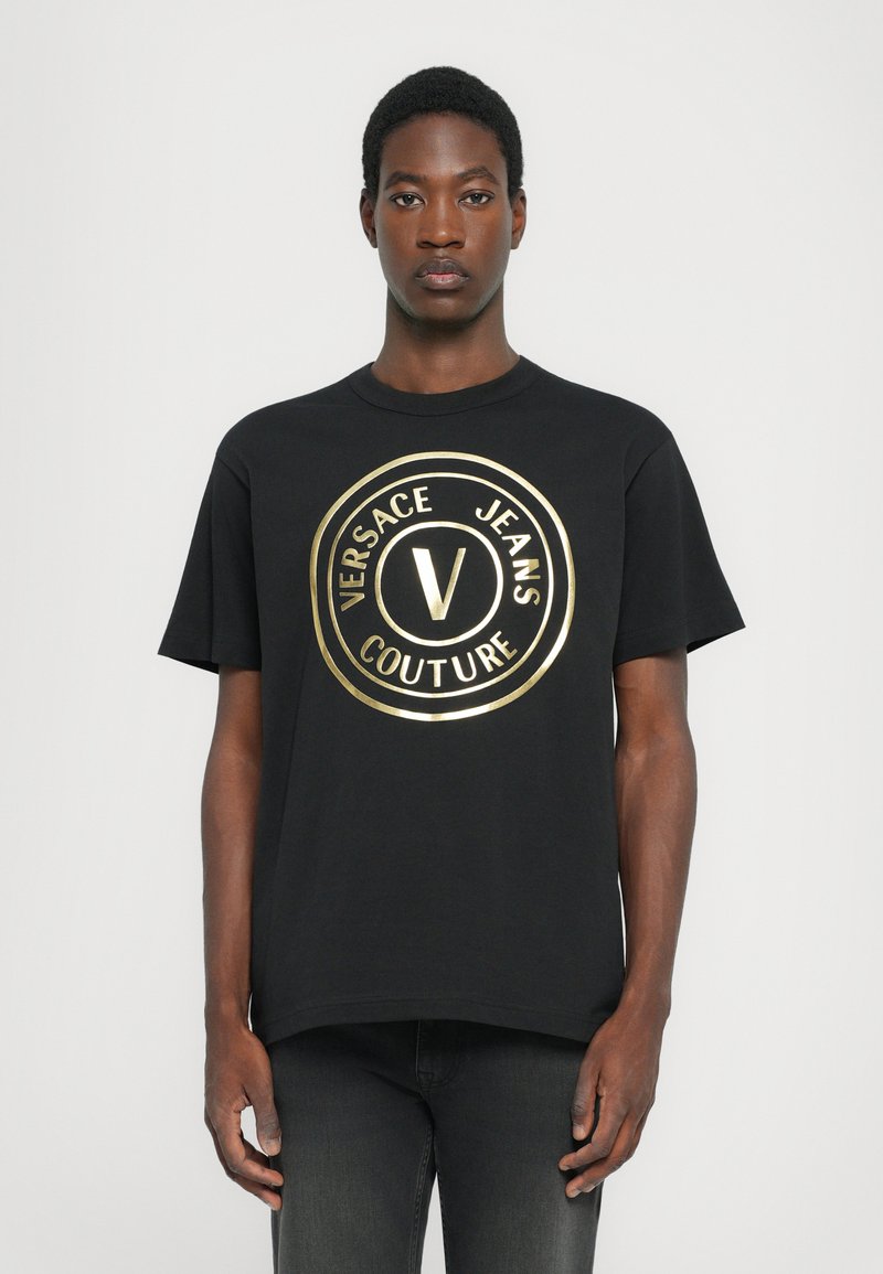 Tricou din bumbac negru, cu un logo circular mare de culoare aurie, având textul "VERSACE JEANS COUTURE" și litera centrală "V". Mâneci scurte, guler rotund.