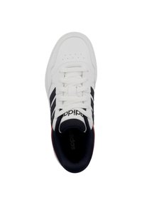 Zapatilla blanca con rayas negras, parte superior de cuero texturizado, lengüeta acolchada y acento rojo en el talón. Presenta cordones blancos planos y puntera perforada.