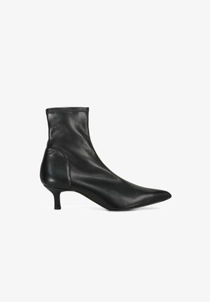 Stivaletto nero in pelle con punta affilata, tacco piccolo kitten e gambale aderente su sfondo bianco.