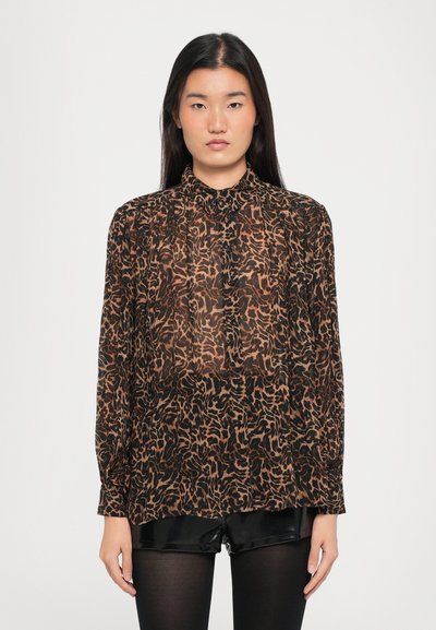 Blouse transparente marron avec un imprimé animal abstrait noir, col montant, fermeture à boutons et manches longues, associée à un short noir.