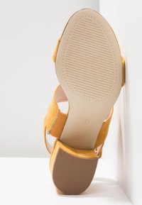 Sandale à talon bloc en suède jaune inclinée pour montrer la semelle lisse avec talon texturé et bride élastique latérale, taille 4, fabriquée en Chine.