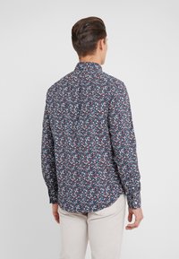 Camicia a maniche lunghe con sfondo blu navy e un motivo floreale multicolore, colletto a bottoni e orlo curvo. Tessuto morbido.